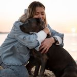 Tutora abraçando seu cachorro na areia da praia