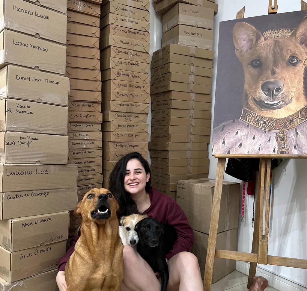 CEO da Cusca Criativa, com seus dois cachorros e um quadro personalizado, em frente às caixas com pedidos dos clientes