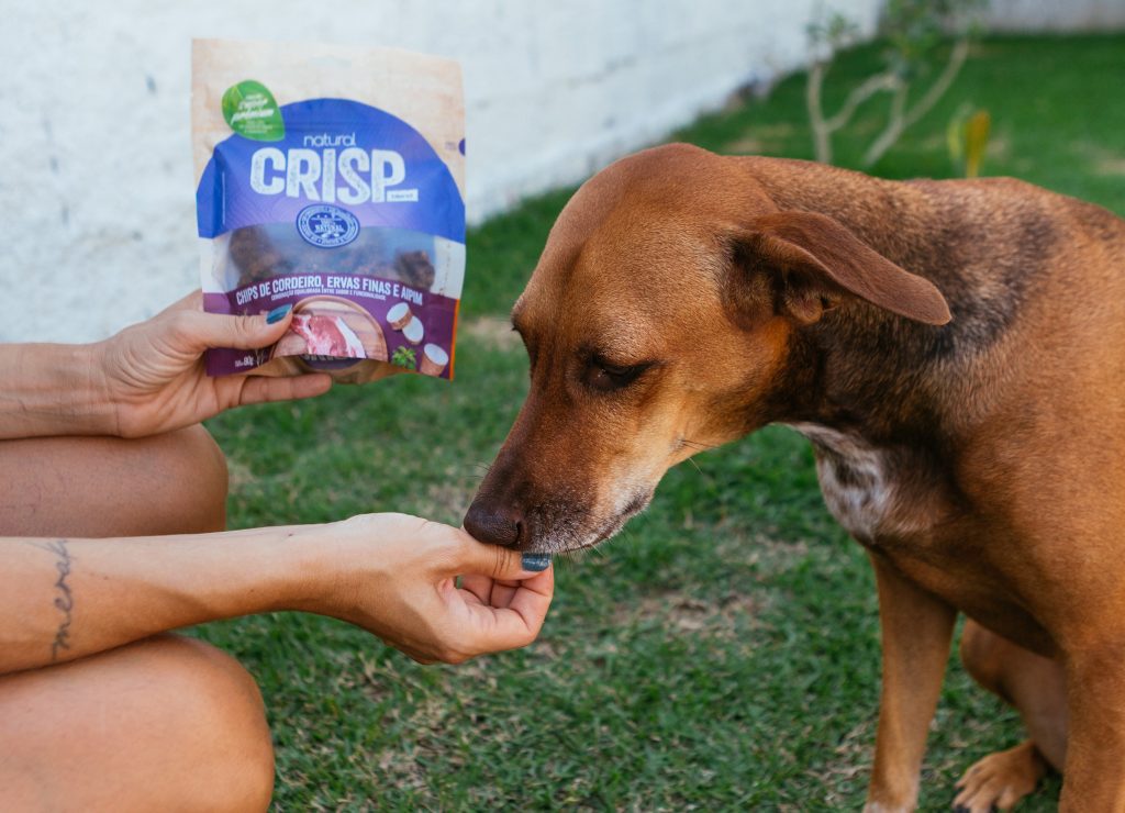 Ao ar livre, tutora oferece Petisco Natural Crisp sabor cordeiro, aipim e ervas finas para seu cachorro