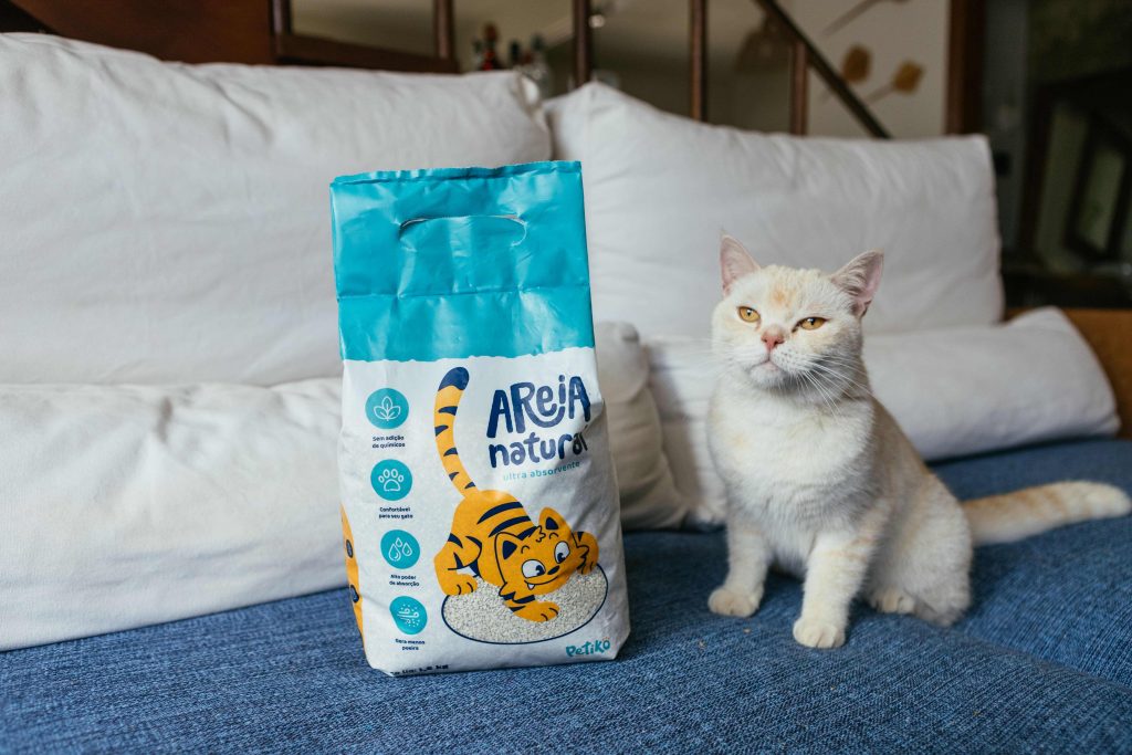 Gato sentado no sofá ao lado de Areia Natural Ultra Absorvente enviada no BOX.Petiko